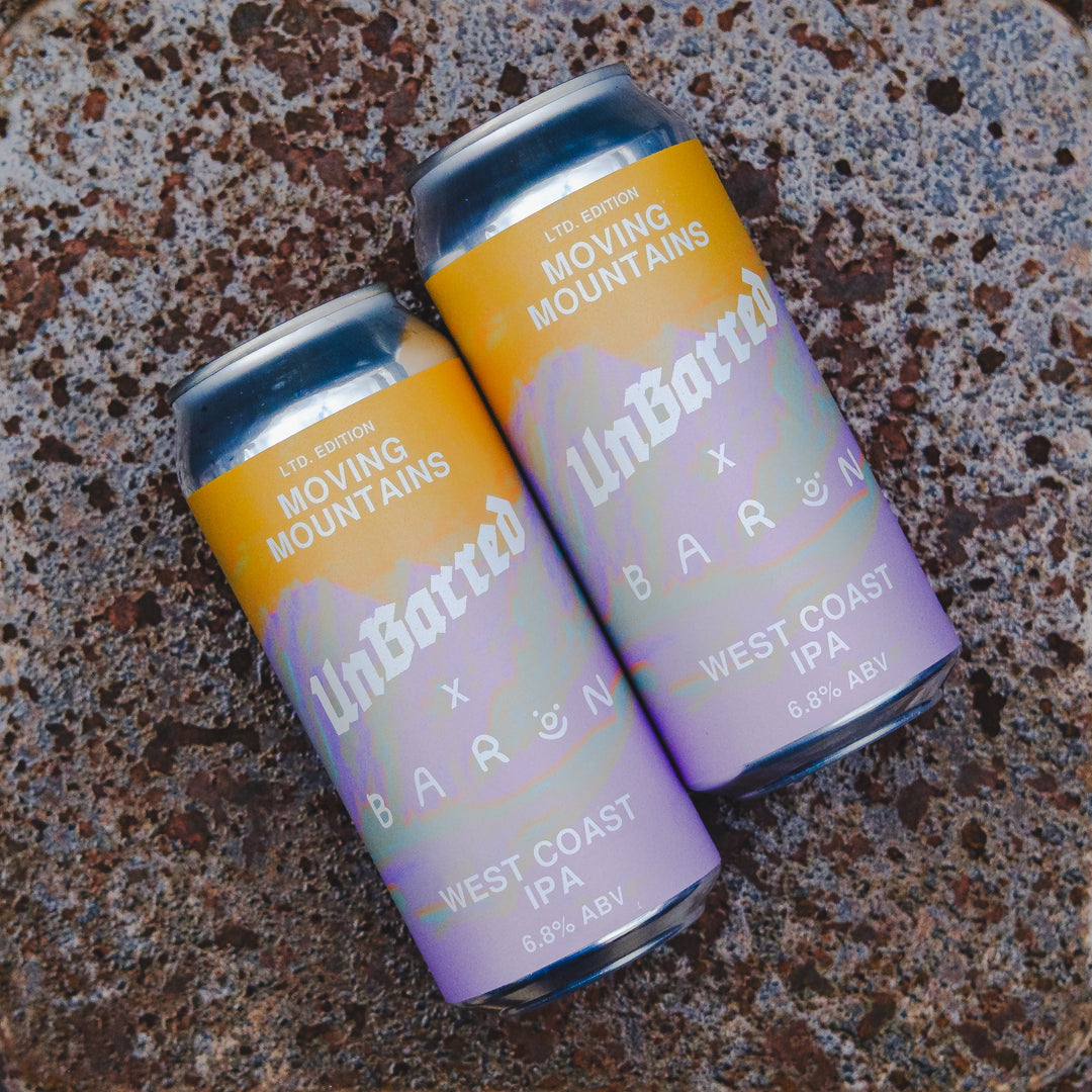 Two aluminum craft beer cans labeled 'UnBatted x BARON Moving Mountains West Coast IPA' resting on a textured speckled surface.