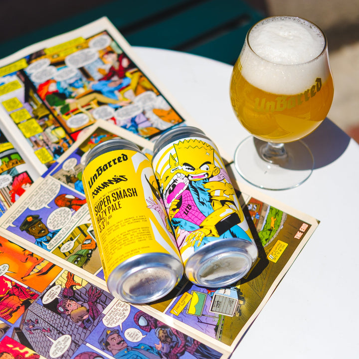 Two cans of 'UnBarred Super Smash' beer on comic book pages with a glass of beer on a table